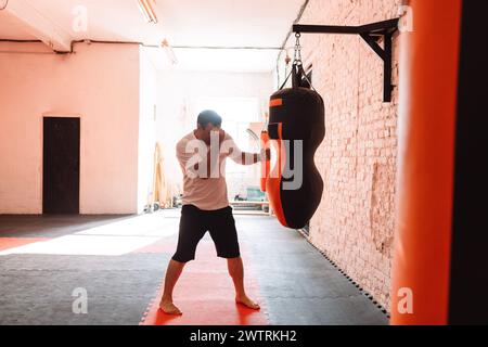 Un giovane uomo sta colpendo un sacco di pugni in palestra. L'atleta è impegnato nel pugilato. Lo sportivo si sta allenando. Interni moderni. Foto Stock