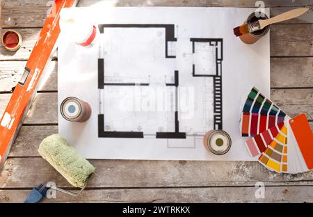 Piano di ristrutturazione della casa su un vecchio tavolo di legno. Vista dall'alto. Foglio di carta con lattine di vernice e pennelli, tavolozza per la scelta dei colori, struttura Foto Stock