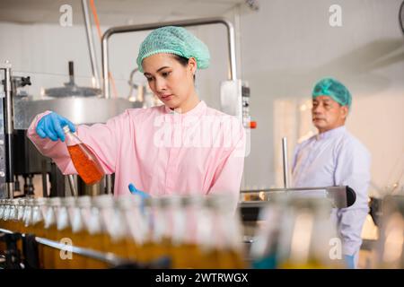 Gli ingegneri QC ispezionano la produzione di bevande a base di succo di frutta in bottiglie di vetro presso la fabbrica Foto Stock