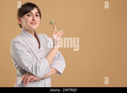 Cosmetologo con rullo facciale su sfondo beige, spazio per testo Foto Stock