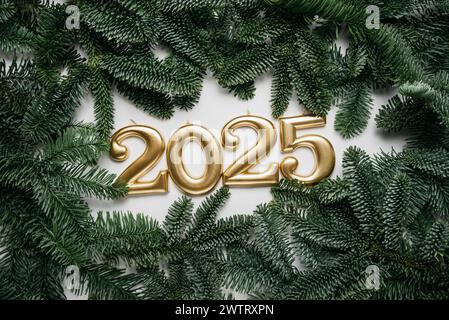 Sfondo festivo felice anno nuovo 2025. Numeri dell'anno 2025 realizzati con candele d'oro sullo sfondo con abete. Festeggiamo le vacanze di Capodanno, primo piano. Spazio per il testo Foto Stock