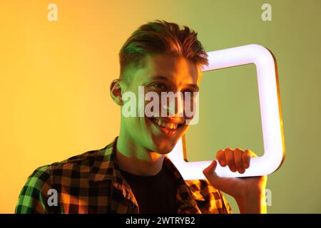 Giovane uomo con lampada quadrata su sfondo colorato con luci al neon Foto Stock