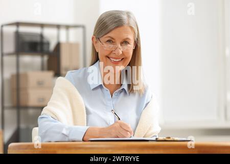 Donna anziana sorridente che firma l'ultimo testamento e il Testamento a tavola in casa Foto Stock