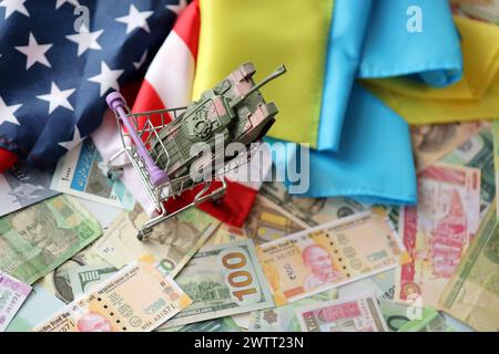 Serbatoio giocattolo sulla bandiera degli Stati Uniti e bandiera ucraina su molte banconote di valuta diversa. Contesto di finanziamento della guerra e sostegno militare tra Stati Uniti e Ucraina Foto Stock