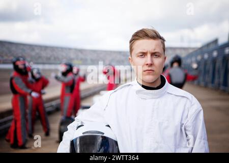 Un giovane pilota concentrato tiene il casco in pista con i concorrenti sullo sfondo Foto Stock