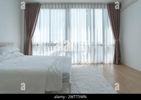 Camera da letto bianca con tende bianche e cuscini bianchi la mattina Foto Stock