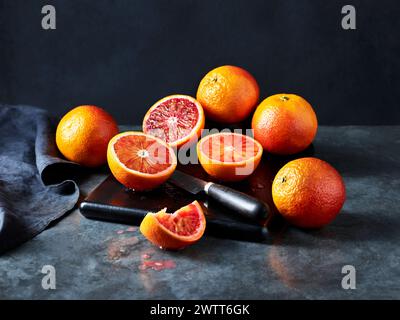 Le arance di sangue sono tagliate a fette su una superficie di cucina scura Foto Stock