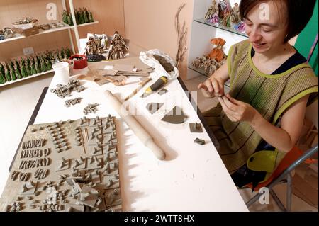 Artista che forma sculture di argilla in un laboratorio pieno di creazioni fatte a mano. Foto Stock