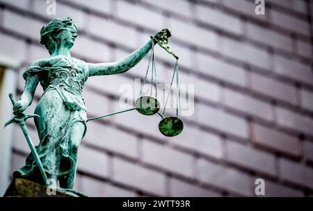 Una statua intemprata di Lady Justice che regge le scale della giustizia sullo sfondo di un edificio sfocato. Foto Stock