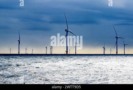 Turbine eoliche che si innalzano sopra il mare scintillante al crepuscolo Foto Stock