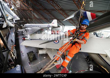 Gli specialisti dell'accesso alla fune industriale si lanciano al Royal Air Force Museum Midlands, a Cosford, vicino a Telford, nello Shropshire, per accedere a una mostra di aerei sospesi esposta nella National Cold War Exhibition, durante la pulizia e la manutenzione annuale di alto livello degli aeromobili. Data foto: Martedì 19 marzo 2024. Foto Stock