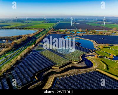 Vista aerea di un'estesa fattoria solare accanto alle turbine eoliche in un paesaggio verde. Foto Stock