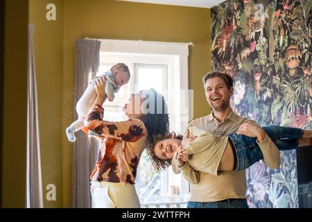 Divertimento per tutta la famiglia come genitore solleva un bambino gioioso in aria in un ambiente accogliente. Foto Stock