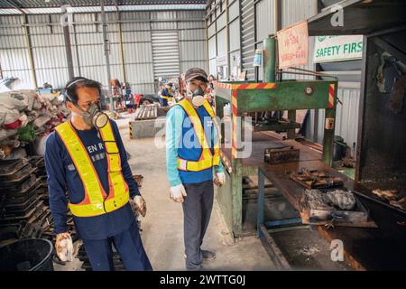 Lavoratori che monitorano i macchinari in una fabbrica di riciclaggio di plastica, Thailandia Foto Stock