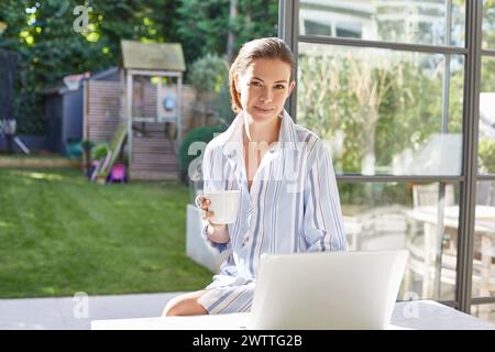 Donna con caffè e notebook in un cortile soleggiato Foto Stock