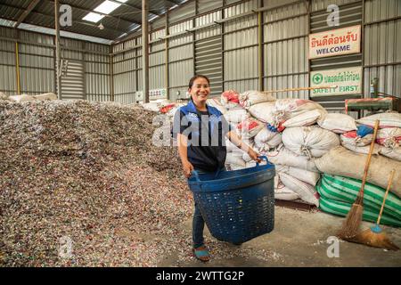 Lavoratore sorridente in mezzo a una montagna di tappi per bottiglie di plastica da riciclare, fabbrica di riciclaggio di plastica, Thailandia Foto Stock