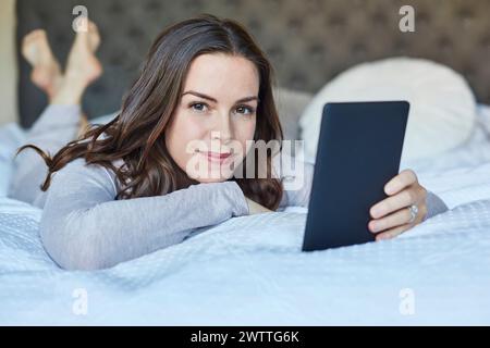 Donna sdraiata a letto che regge un tablet Foto Stock