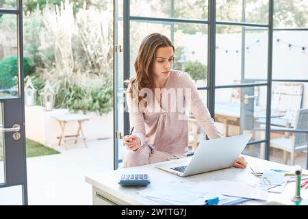 Donna che lavora su un notebook in un luminoso ufficio domestico Foto Stock