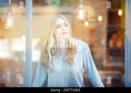 Donna che guarda fuori da una finestra con le lampadine. Foto Stock