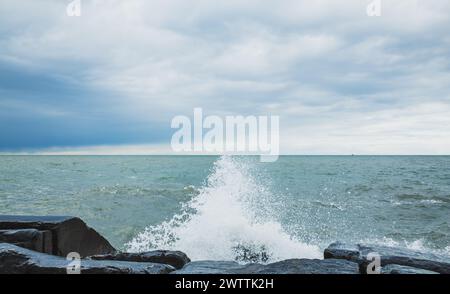 Le tempeste onde oceaniche si schiantano contro la costa rocciosa frastagliata sotto il cielo nuvoloso Foto Stock