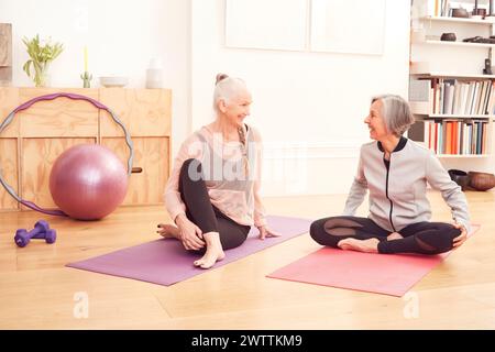 Due donne sorridenti e sedute su tappetini da yoga Foto Stock