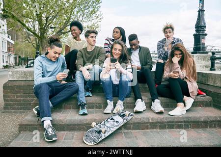 Gruppo di giovani con smartphone seduti su una panchina Foto Stock