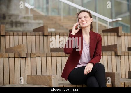 Donna che parla al telefono mentre è seduta sulle scale all'aperto. Foto Stock