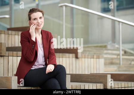 Donna che parla al telefono mentre è seduta sulle scale Foto Stock