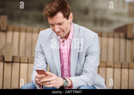 Uomo in un blazer che usa uno smartphone su scale all'aperto. Foto Stock