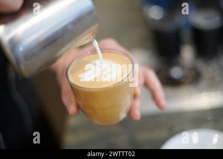 Il barista versa il latte nel caffè, creando latte art Foto Stock