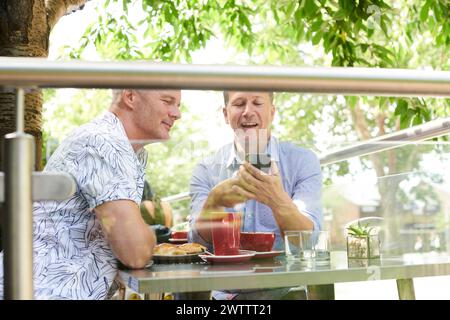 Due uomini che si godono un pasto e guardano uno smartphone Foto Stock