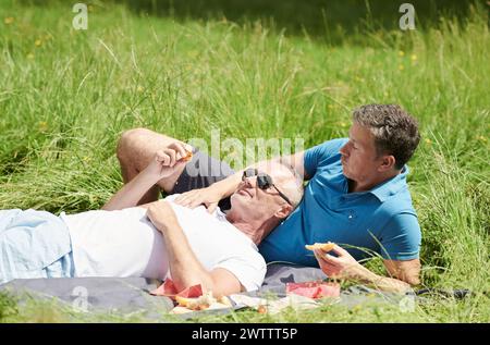 Due uomini che si godono un picnic in una giornata di sole sull'erba Foto Stock