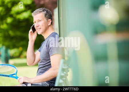 Uomo con una racchetta da tennis che parla al telefono all'aperto Foto Stock