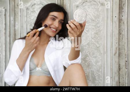 Donna che applica il trucco mentre sorride allo specchio Foto Stock