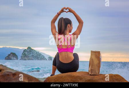 Donna che fa forma al cuore con le mani in spiaggia Foto Stock