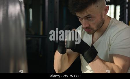 Primo piano pugile caucasico pugile uomo di allenamento box combattimento pugni utilizzare attrezzature sportive. Sportivo forte e motivato che colpisce la borsa da combattimento con un colpo di pugno Foto Stock