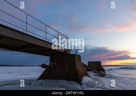 Il vecchio molo rotto si trova sotto il cielo del tramonto in una serata d'inverno, vista prospettica Foto Stock