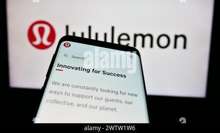 Telefono cellulare con pagina web della società canadese di vendita al dettaglio di abbigliamento Lululemon Athletica Inc. Davanti al logo. Mettere a fuoco in alto a sinistra sul display del telefono. Foto Stock