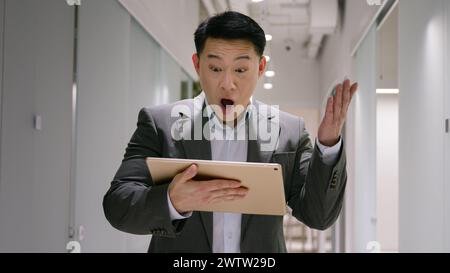 Felice eccitato uomo d'affari asiatico di mezza età cinese coreano giapponese uomo con tablet digitale vincere successo di affari scommessa lotteria di soldi stupito 40s maschio Foto Stock