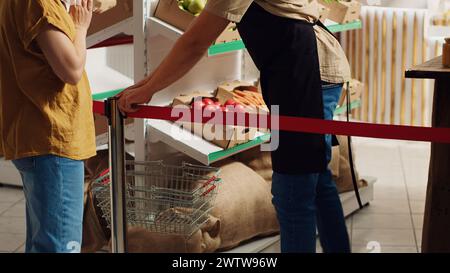 Il fornitore saluta i primi clienti nel nuovo supermercato zero rifiuti, rimuovendo il nastro rosso. Il negoziante accoglie gli acquirenti all'interno di un negozio di quartiere ecologico Foto Stock