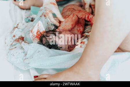 Immagine di nascita autentica: Una bambina appena nata piangente con i capelli scuri coperti di sangue pochi istanti dopo la nascita. Cordone ombelicale ancora attaccato. Foto Stock