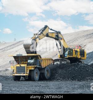 grande dumper da miniera giallo e escavatore che lavora in cava. Carico di carbone nel dumper. Foto Stock