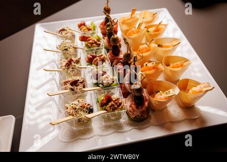 Una presentazione gourmet di stuzzichini assortiti, con succulenti gamberi e una varietà di deliziosi spuntini, serviti elegantemente su un piatto bianco. Foto Stock