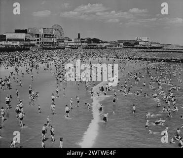 Vista sopraelevata lungo la costa che mostra una spiaggia affollata e l'oceano a Coney Island, New York, Luna Park può essere visto sullo sfondo Foto Stock