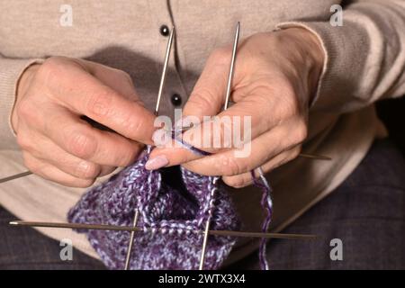 Le mani delle donne stanno lavorando un calzino caldo con quattro aghi per maglieria. Foto Stock