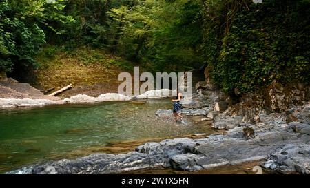 Donna escursionista che corre nel fiume in una splendida giornata estiva. Creatività. Serbatoio d'acqua Paradise nella giungla. Foto Stock