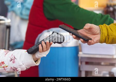 Corpo centrale di una donna che tiene in mano un telefono cellulare e che effettua un pagamento online su un terminale, vista ravvicinata e ad angolo basso presso la fiera dello Street food di Praga Foto Stock