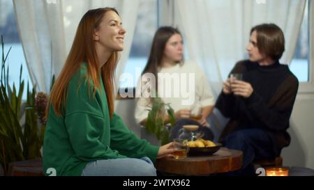 Vista laterale di una donna felice e rilassata che si gusta il tè e sembra da sogno. Supporto. Coppia sfocata che comunica sullo sfondo. Foto Stock