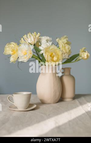 Mazzo di gerbera gialla, tulipani e ranunculus in un vaso con ceramiche assortite su un tavolo alla luce del sole Foto Stock