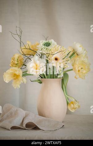 Mazzo di fiori gialli di gerbera, tulipani e ranunculus in un vaso su un tavolo con un tovagliolo Foto Stock
